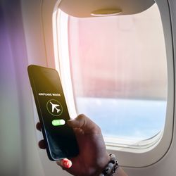 hand holding phone switching to airplane mode with airplane window in background