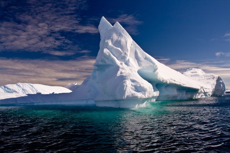 Large white iceberg above water, against a blue sky.