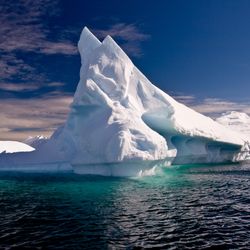 Large white iceberg above water, against a blue sky.