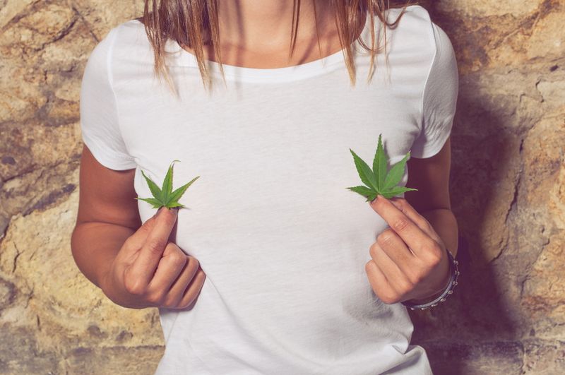 A woman in a white top holding two cannabis leafs.
