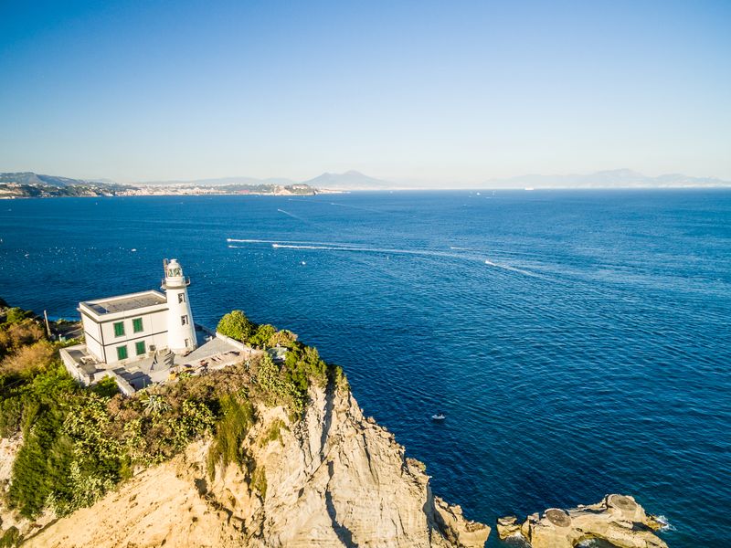 Capo Miseno Lighthouse at one edge of the bay of Pozzuoli, Naples and Vesuvius on background