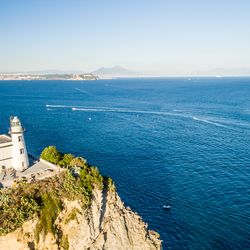 Capo Miseno Lighthouse at one edge of the bay of Pozzuoli, Naples and Vesuvius on background