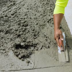 A photo of freshly poured concrete being shaped by a construction worker. 