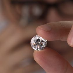 man expert buyer with glasses evaluates polished diamond trough magnifying glass close up.