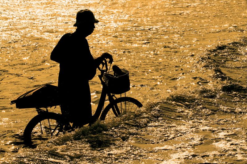 A silhouette of a old man and his bicycle getting caught in a flash flood following ran. 