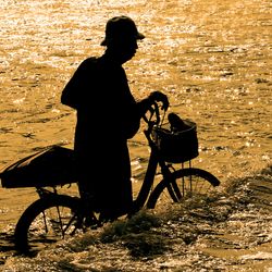 A silhouette of a old man and his bicycle getting caught in a flash flood following ran. 