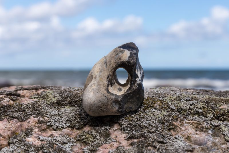 hag stone sitting on a larger rock, the sky visible through the hole