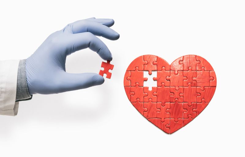Hand in a blue latex glove placing a red puzzle piece into a heart-shaped puzzle that is missing one piece