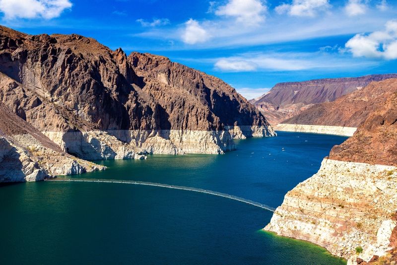 A photo of lake mead surrounded by high cliffs that show a distinct line that separates the old water levels with the brown cliffs 