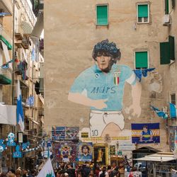 A busy city streety in Naples, Italy, with a graffiti portrait of Maradona on the wall.