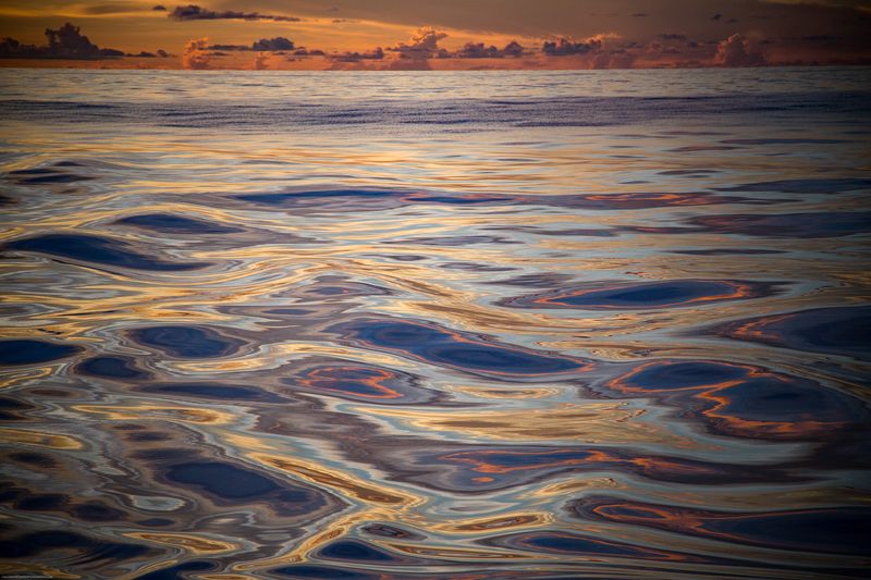 Ripples on top of the ocean surface with a sunset sky in the background.