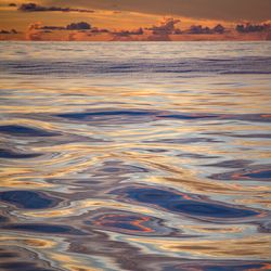 Ripples on top of the ocean surface with a sunset sky in the background.