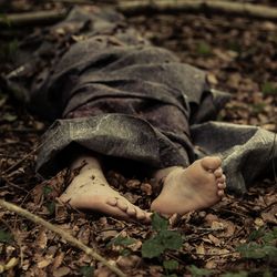 Person wrapped in grey blanket on forest floor, feet protruding from bottom of blanket