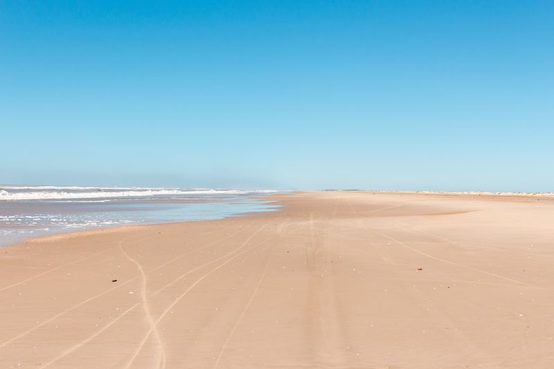 A stretch of Praia do Cassino on a clear blue sky day.