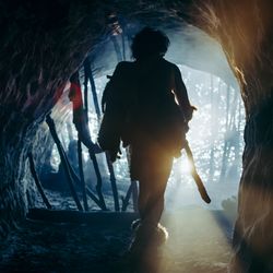 The silhouetted back of a man dressed like an early human is seen leaving a cave.